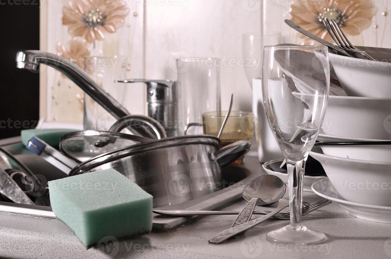 A huge pile of unwashed dishes in the kitchen sink and on the countertop photo