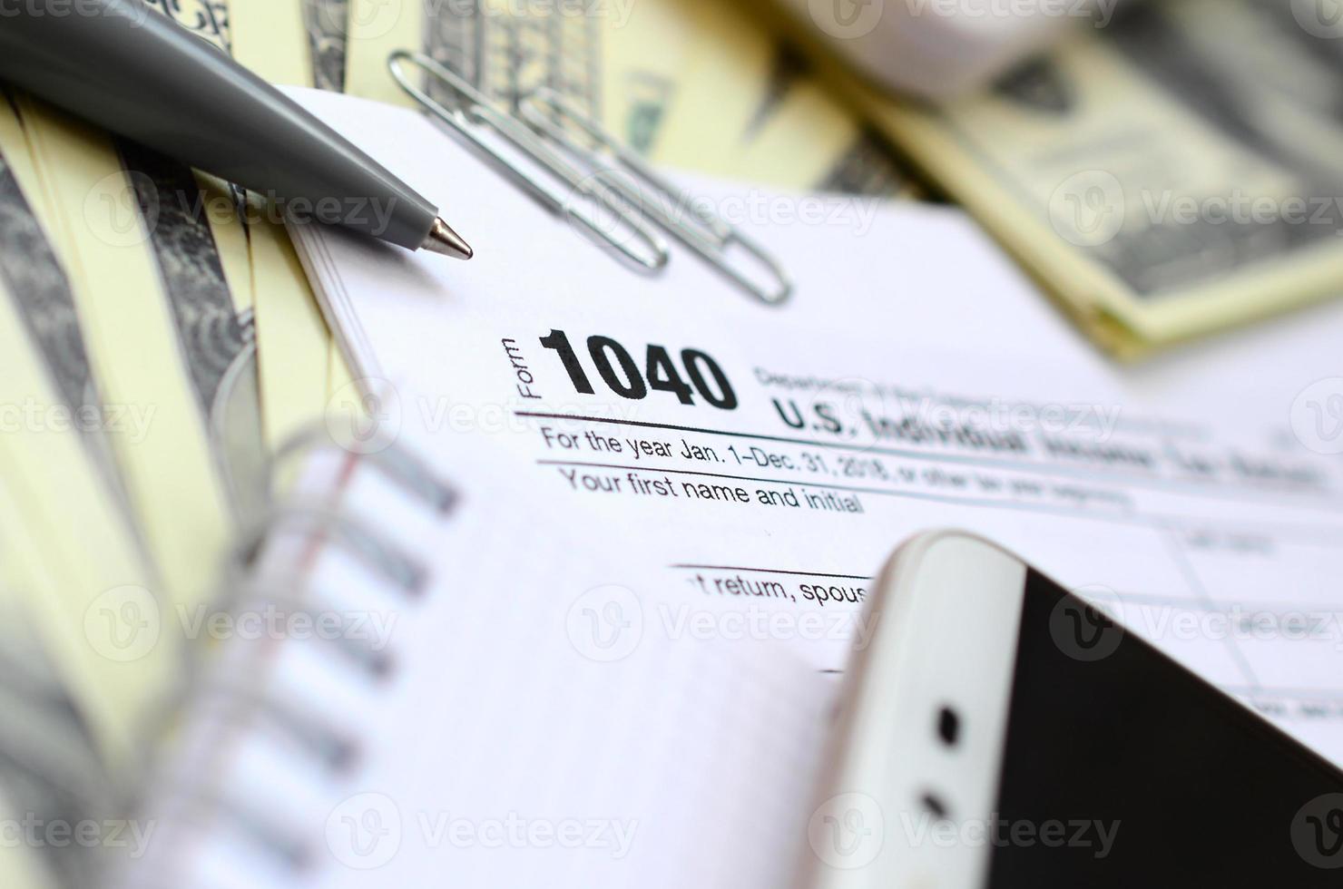 The pen, notebook, calculator, smartphone and dollar bills is lies on the tax form 1040 U.S. Individual Income Tax Return. The time to pay taxes photo