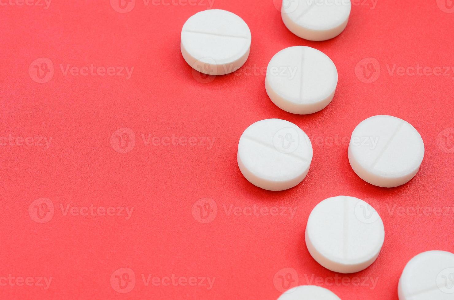 A few white tablets lie on a bright red background surface. Background image on medical and pharmaceutical topics photo