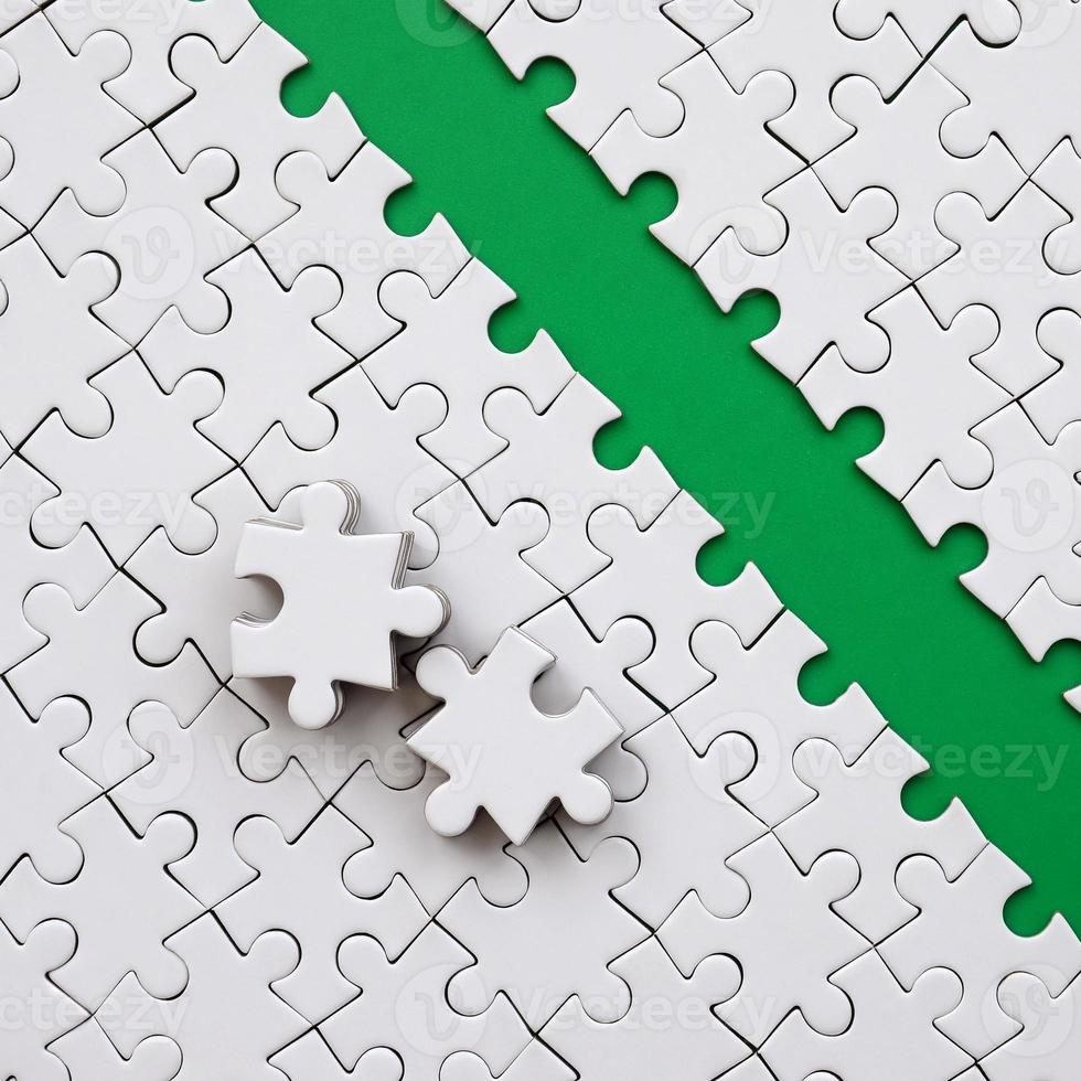 The green path is laid on the platform of a white folded jigsaw puzzle. The missing elements of the puzzle are stacked nearby. Texture image with space for text photo