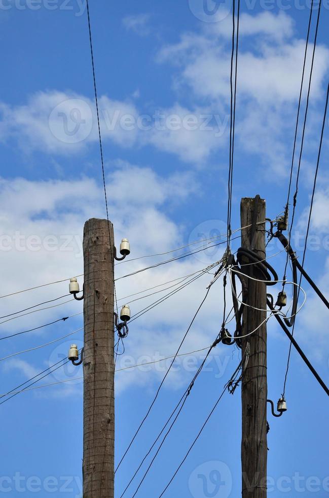 Old wooden electric pole for transmission of wired electricity on a background of a cloudy blue sky. Obsolete method of supplying electricity for later use photo