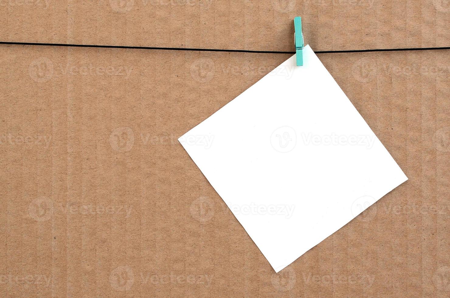 White blank card on rope on a brown cardboard background. Creative reminder, small sheet of paper on wooden clothespin, memo backdrop photo