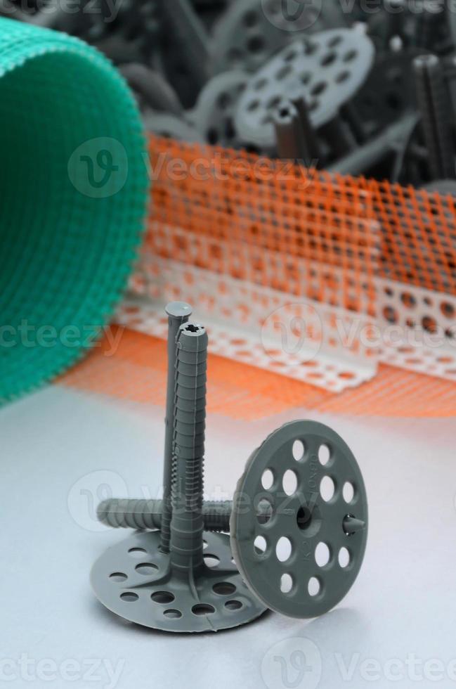 A set of construction items for the insulation of walls. Plastic dowels, a roll of mesh for the insulation of facades and a corner profile with a grid lie on the foam polystyrene surface photo