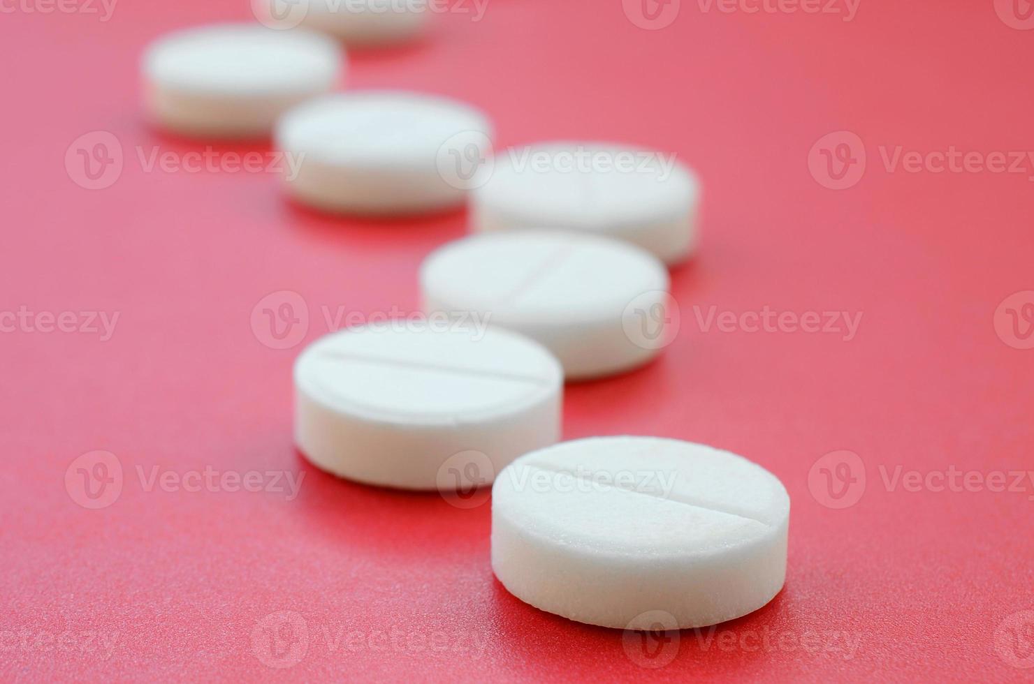A few white tablets lie on a bright red background surface. Background image on medical and pharmaceutical topics photo