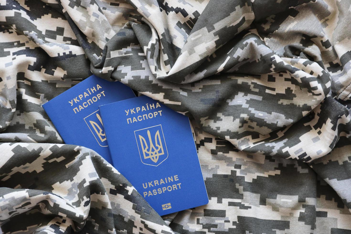 SUMY, UKRAINE - MARCH 20, 2022 Ukrainian foreign passport on fabric with texture of military pixeled camouflage. Cloth with camo pattern in grey, brown and green pixel shapes and Ukrainian ID photo