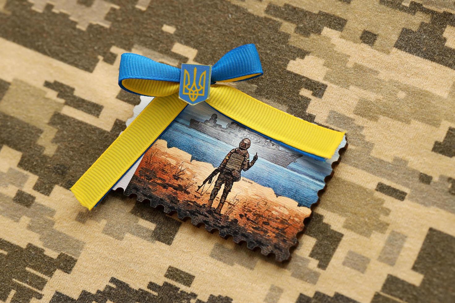 TERNOPIL, UKRAINE - SEPTEMBER 2, 2022 Famous Ukrainian postmark with russian warship and ukrainian soldier as wooden souvenir on army camouflage uniform photo