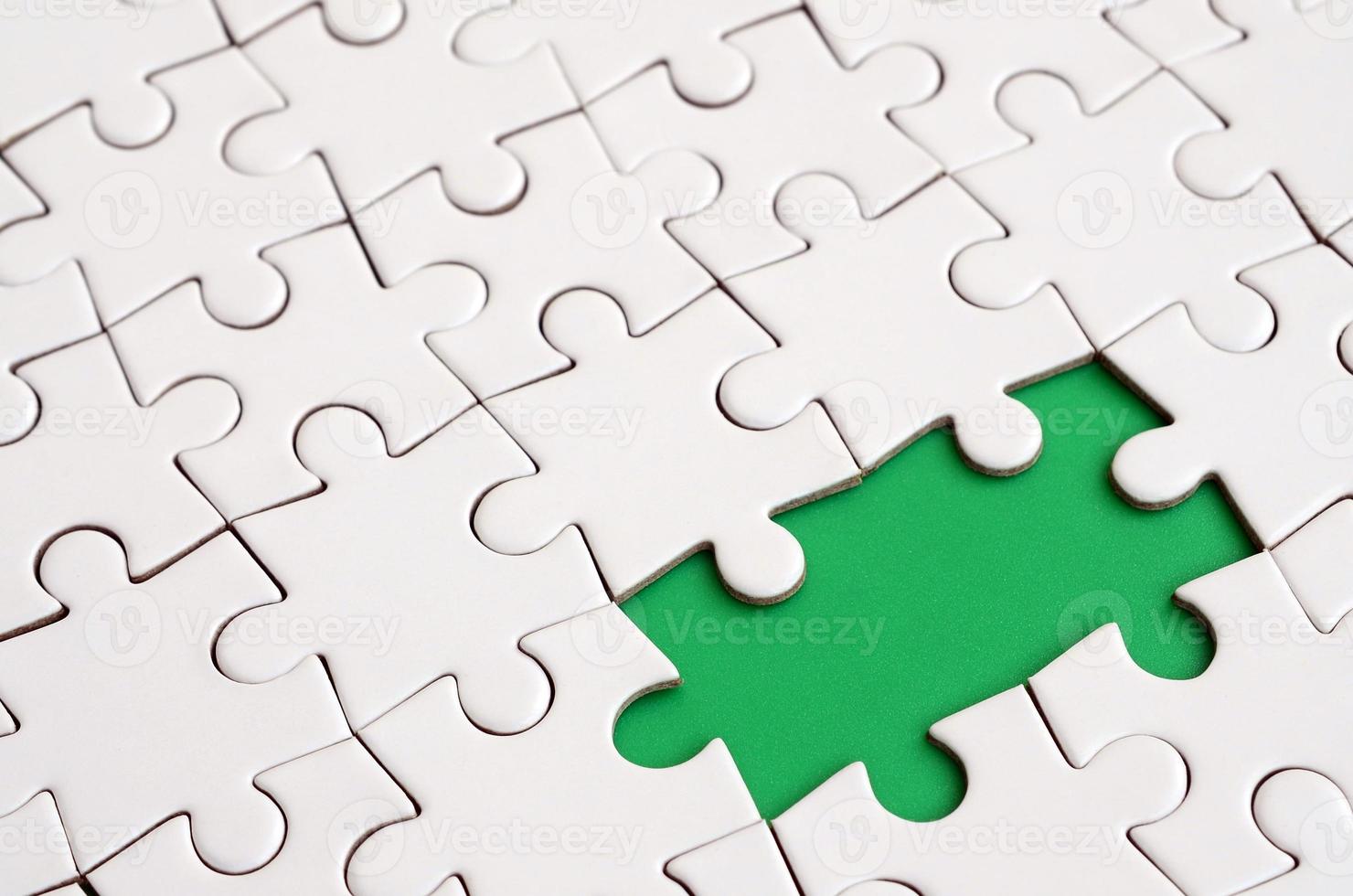 Close-up texture of a white jigsaw puzzle in assembled state with missing elements forming a green pad for text. Copy space photo