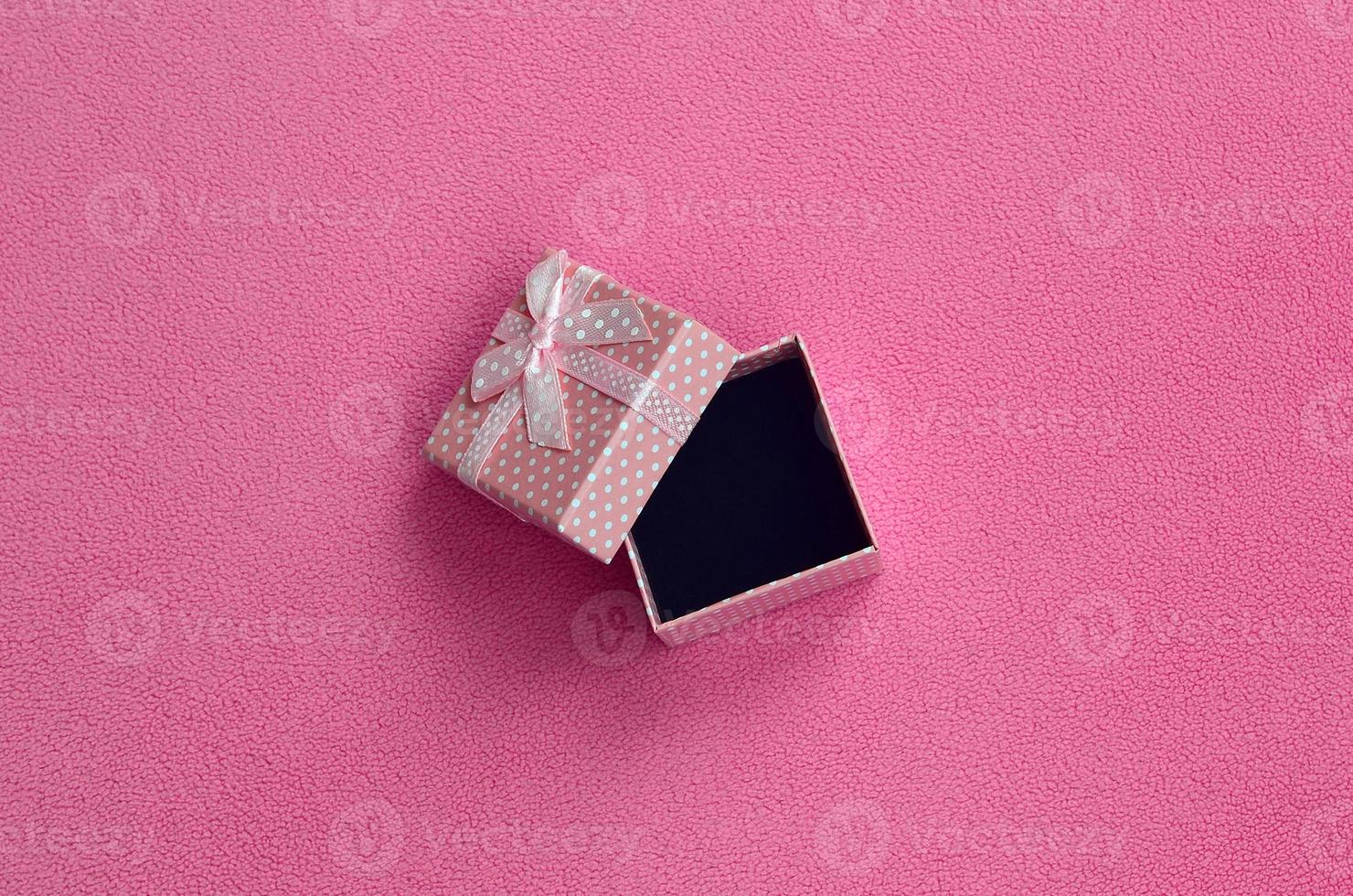 Open small gift box in pink with a small bow lies on a blanket of soft and furry light pink fleece fabric. Packing for a gift to your lovely girlfriend photo
