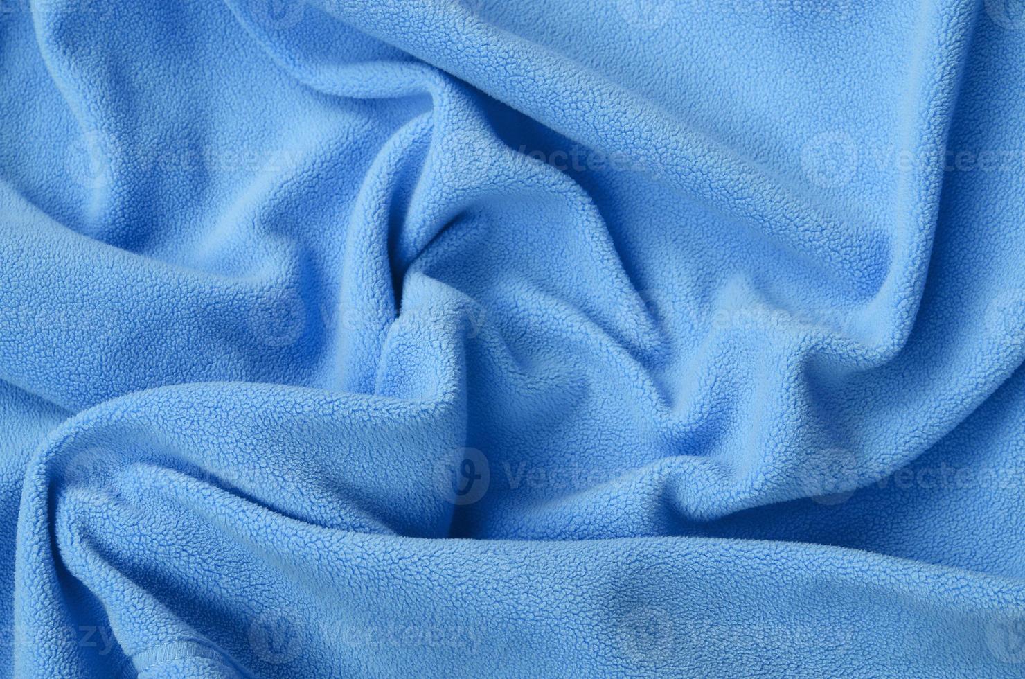 The blanket of furry blue fleece fabric. A background of light blue soft plush fleece material with a lot of relief folds photo