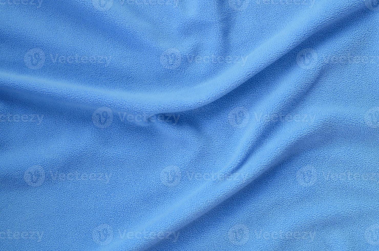 The blanket of furry blue fleece fabric. A background of light blue soft plush fleece material with a lot of relief folds photo