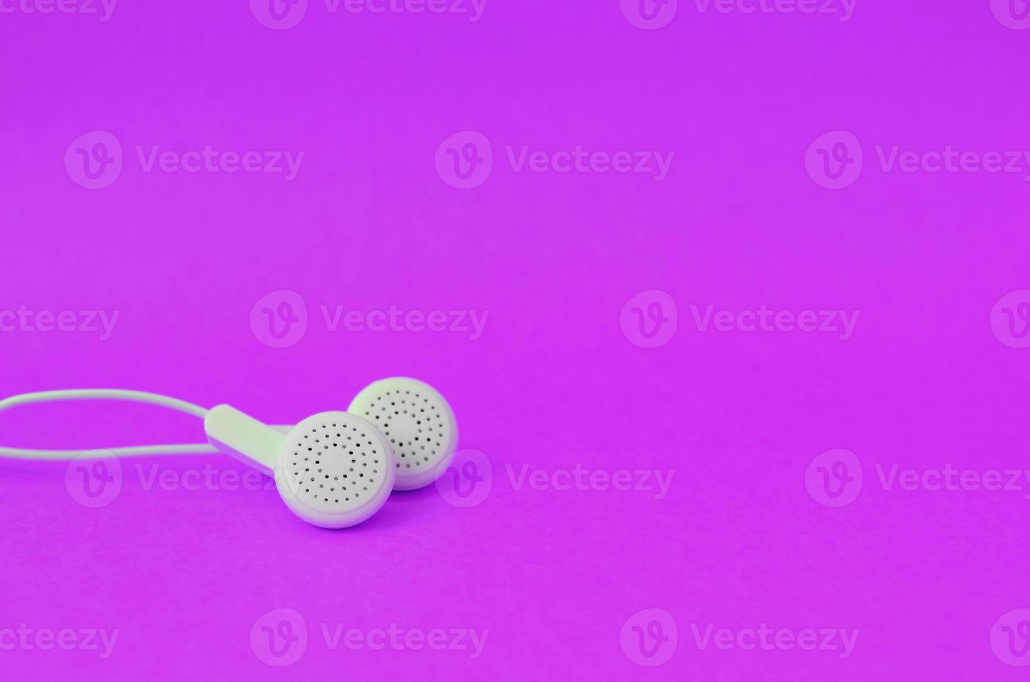 White modern earphones lies on a bright purple background. photo