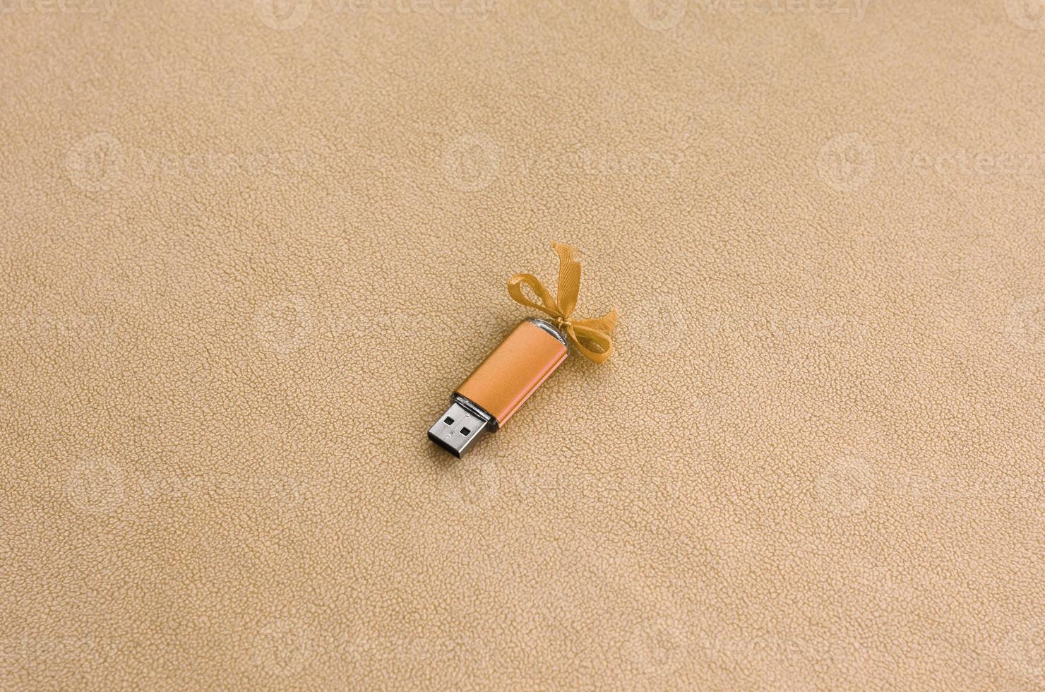 Orange usb flash memory card with a blue bow lies on a blanket of soft and furry light orange fleece fabric. Classic female gift design for a memory card photo