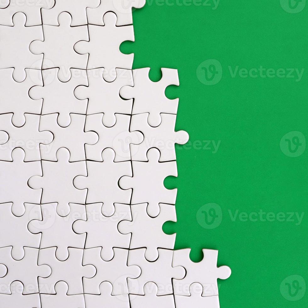 Fragment of a folded white jigsaw puzzle on the background of a green plastic surface. Texture photo with copy space for text