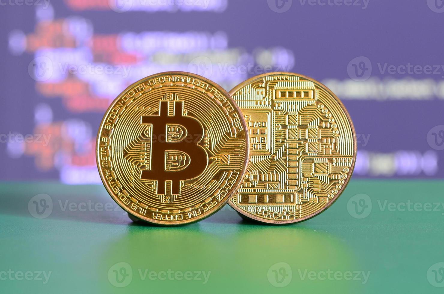 Two gold bitcoins lie on the green surface on the background of the display, which shows the process of mining the crypto currency photo