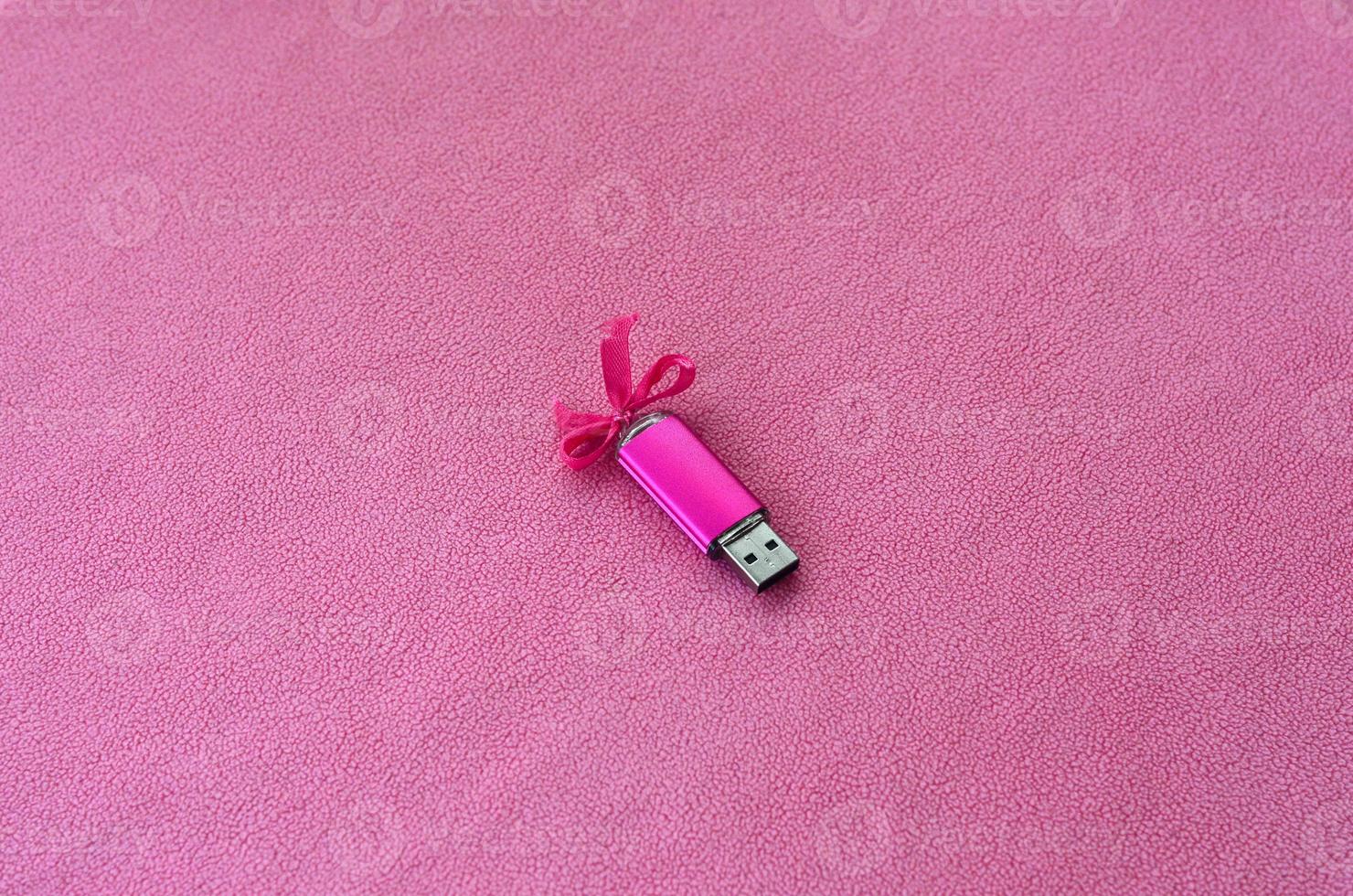 la tarjeta de memoria flash usb de color rosa brillante con un lazo rosa yace sobre una manta de suave y peluda tela de vellón rosa claro. diseño clásico de regalo femenino para una tarjeta de memoria foto
