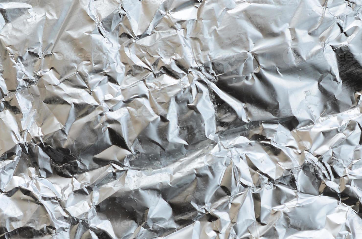 Thin wrinkled sheet of crushed tin aluminum silver foil background with shiny crumpled surface for texture photo