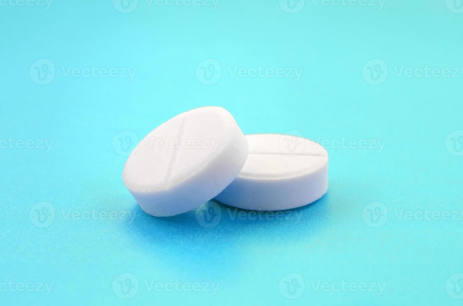 A few white tablets lie on a bright blue background surface. Background image on medical and pharmaceutical topics photo