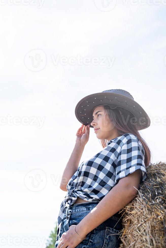 beautiful woman in plaid shirt and cowboy hat resting on haystack photo