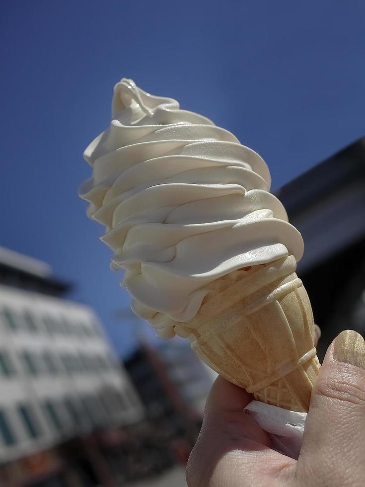 Low angle view, close up a hand holding  soft cream in waffle cone on summer, blurry background of blue bright sky, copy space photo