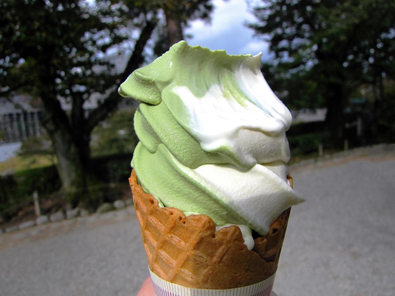 A hand holding melting ice cream waffle cone in hand, green tea matcha, vanilla, on summer , blurry background, copy space photo