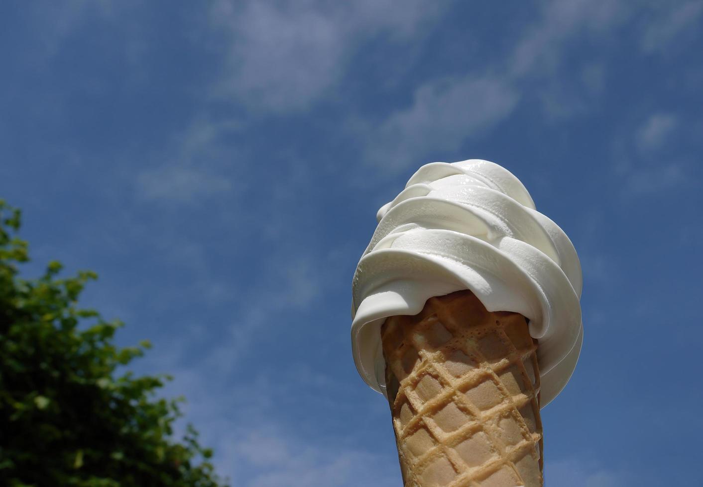 Low angle view, close up a cold soft cream in waffle cone on summer , blurry background of blue bright sky, copy space photo