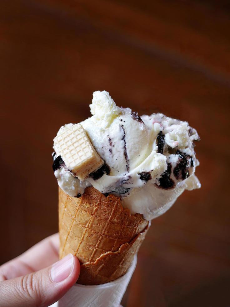 Close up a hand holding Blueberry Cheesecake flavored ice cream in waffle cone, blurry background, focus on foreground photo