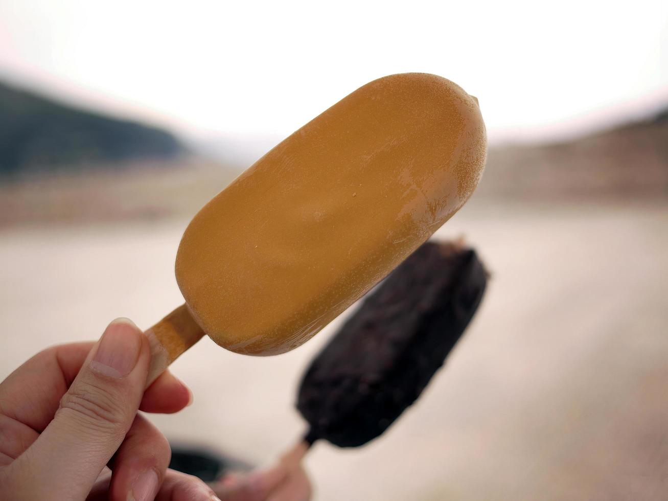 Two hands holding popsicle ice cream sticks different flavors in hands, on summer, dry weather, blurry background photo