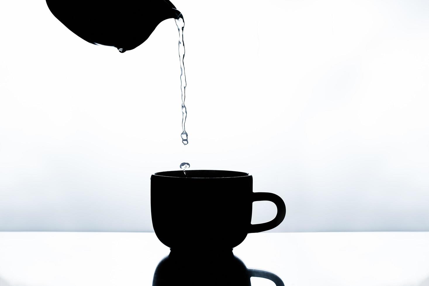 Silhouette of pouring water onto a coffee cup in the morning light photo