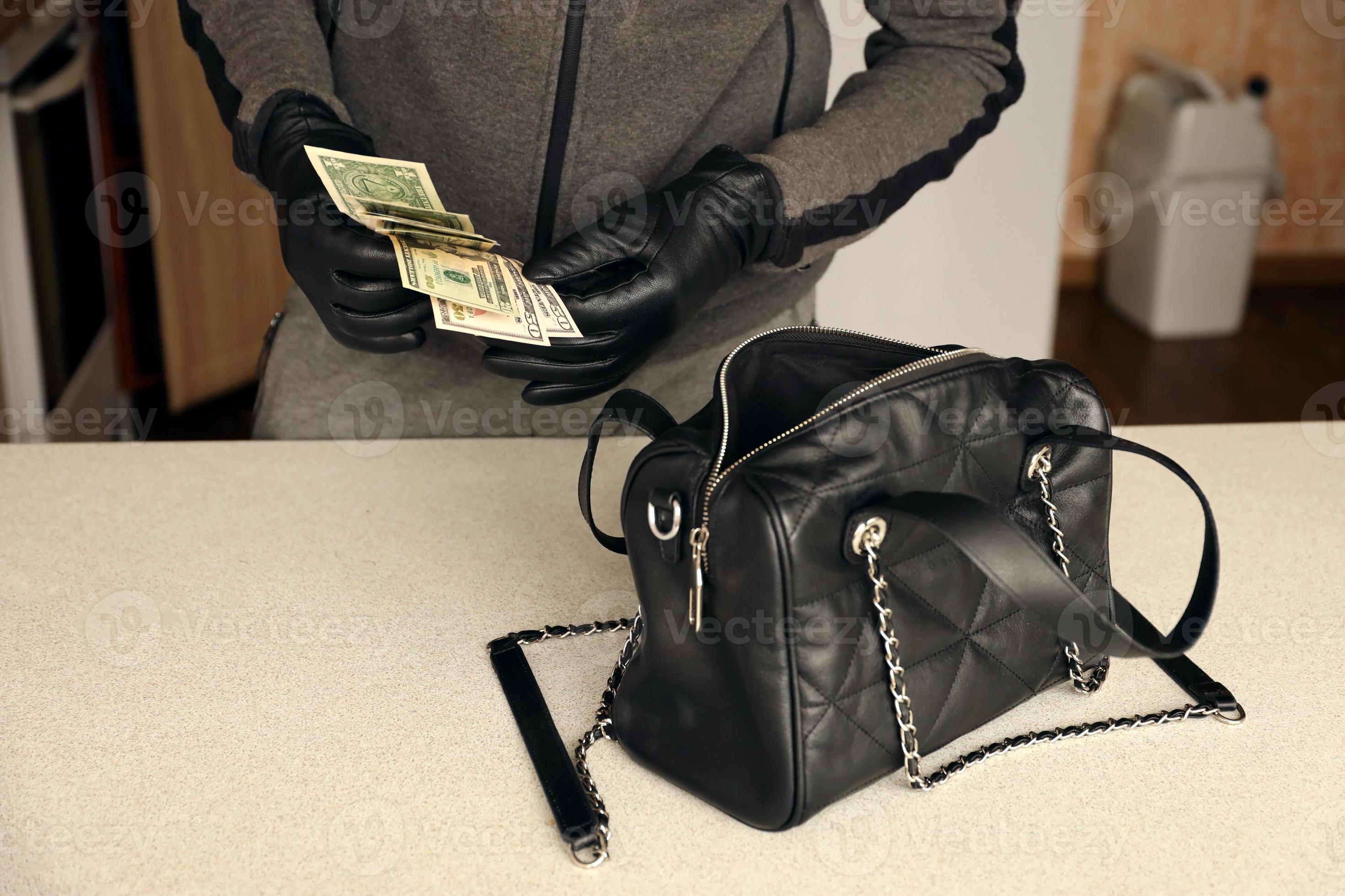 Robber in black outfit and gloves see in opened stolen women bag. The thief  takes out US dollar bills from a womans handbag in kitchen 12345872 Stock  Photo at Vecteezy