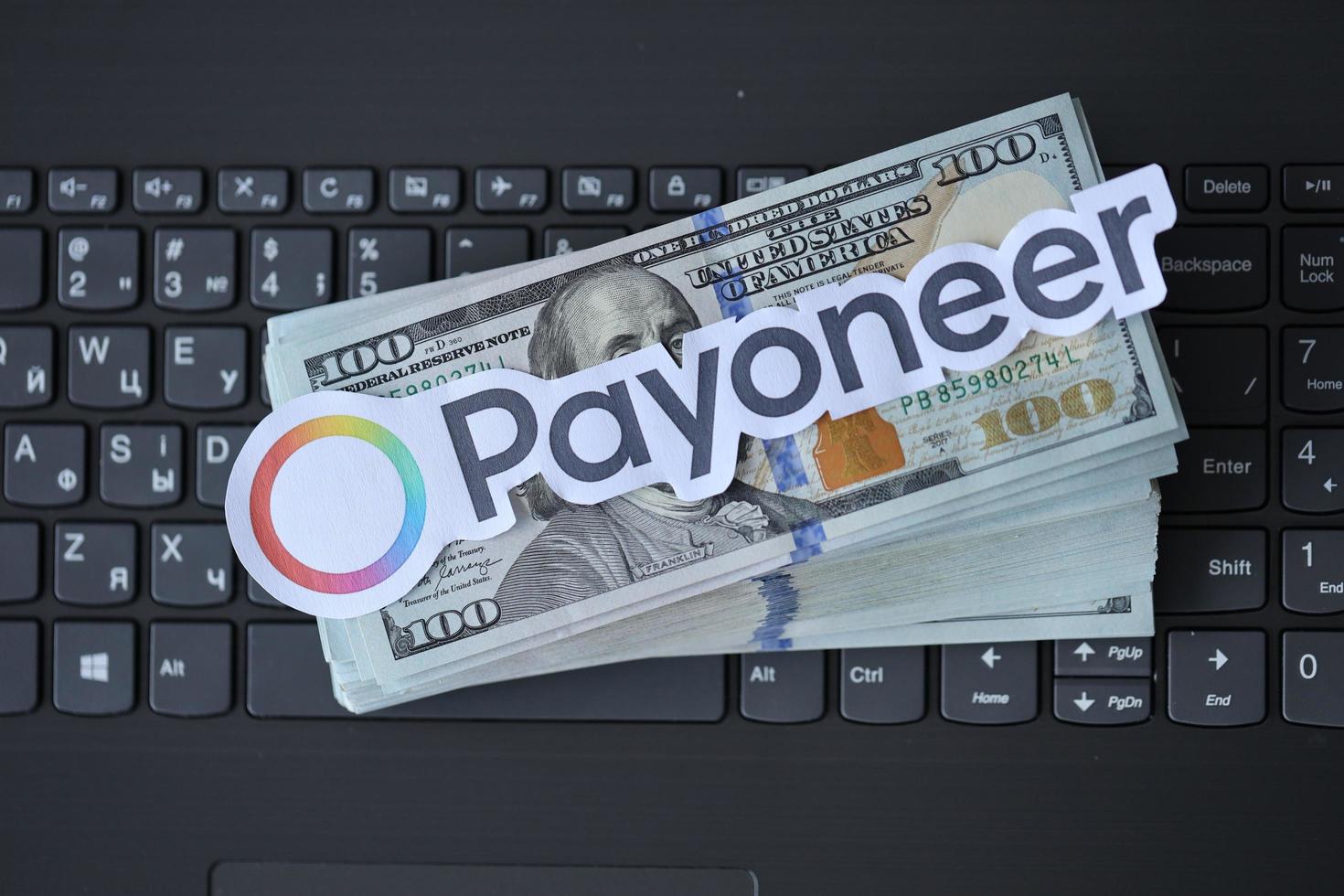 TERNOPIL, UKRAINE - SEPTEMBER 6, 2022 Payoneer paper logotype lies on black laptop with US dollar bills. Payoneer is American financial services company that provides online money transfer photo