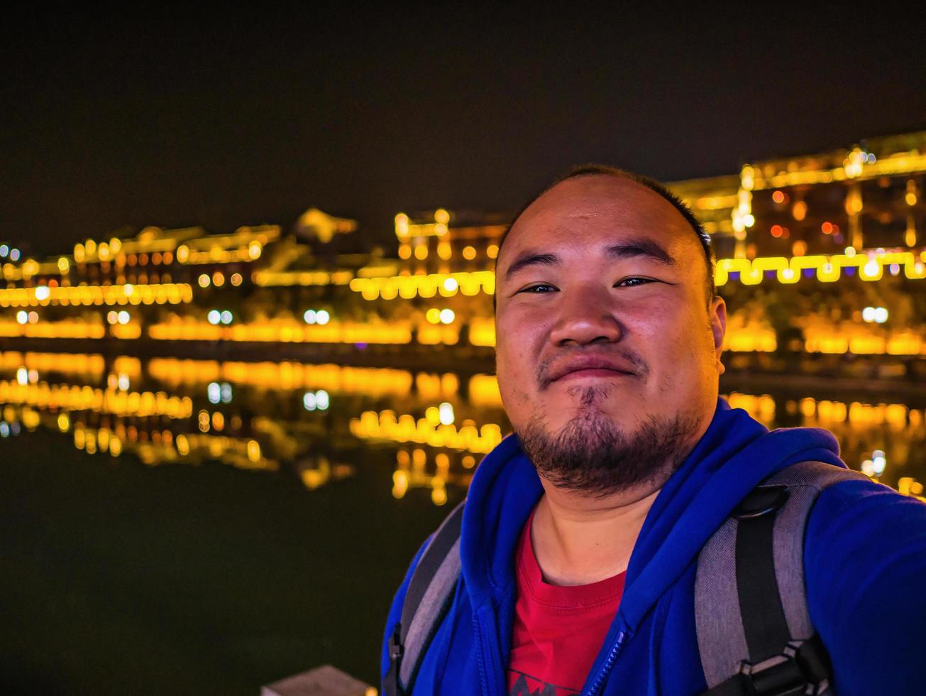 foto de retrato de un mochilero gordo asiático con una hermosa vista del paisaje en la noche del casco antiguo de fenghuang. La ciudad antigua de Phoenix o el condado de fenghuang es un condado de la provincia de Hunan, China