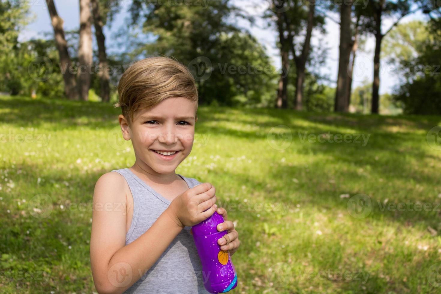 retrato de niño lindo con botella de agua en el parque. foto