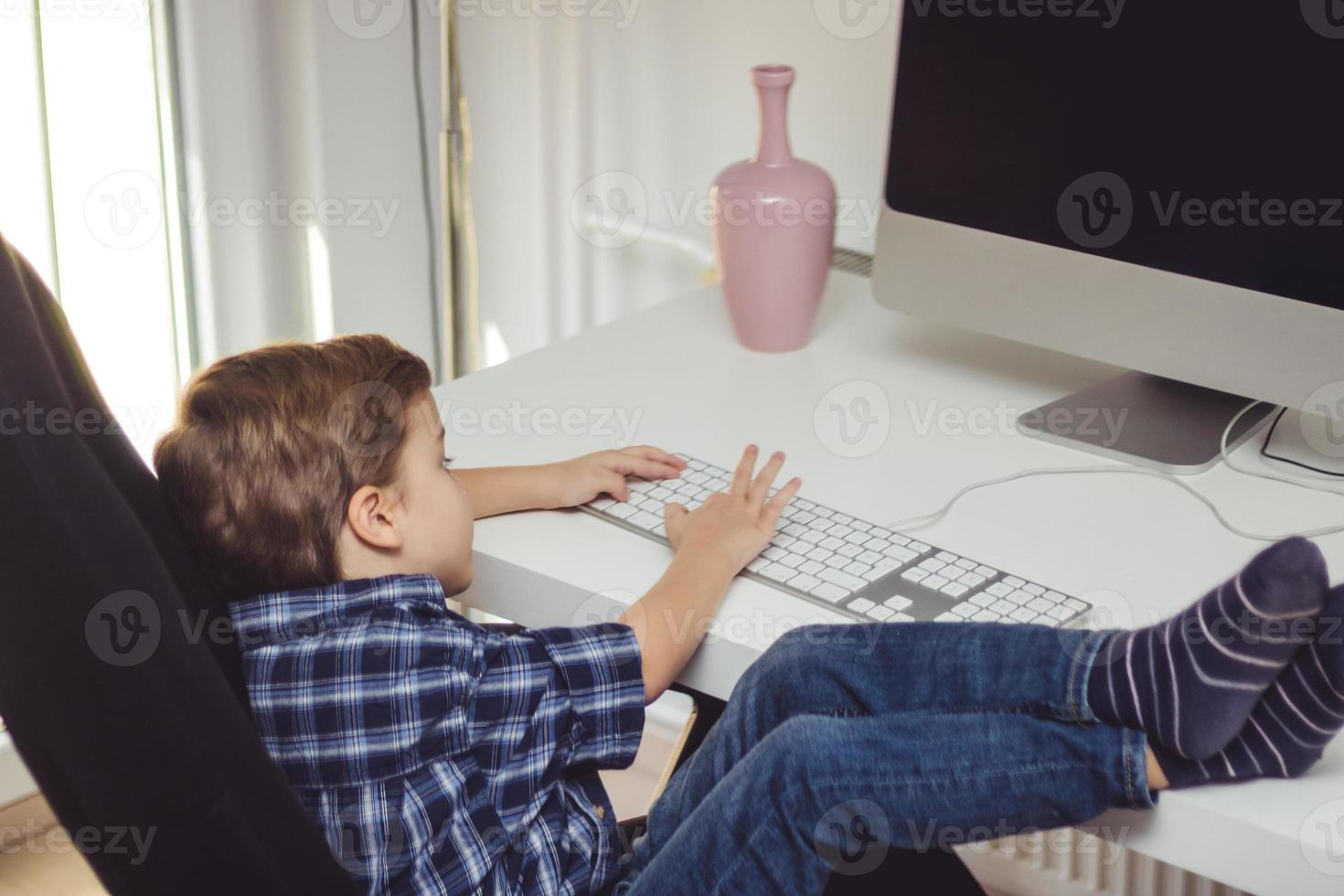 niño pequeño escribiendo en el teclado mientras usa la computadora de escritorio en casa. foto