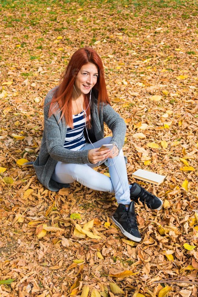 chica pelirroja sonriente relajándose en las hojas de otoño. foto