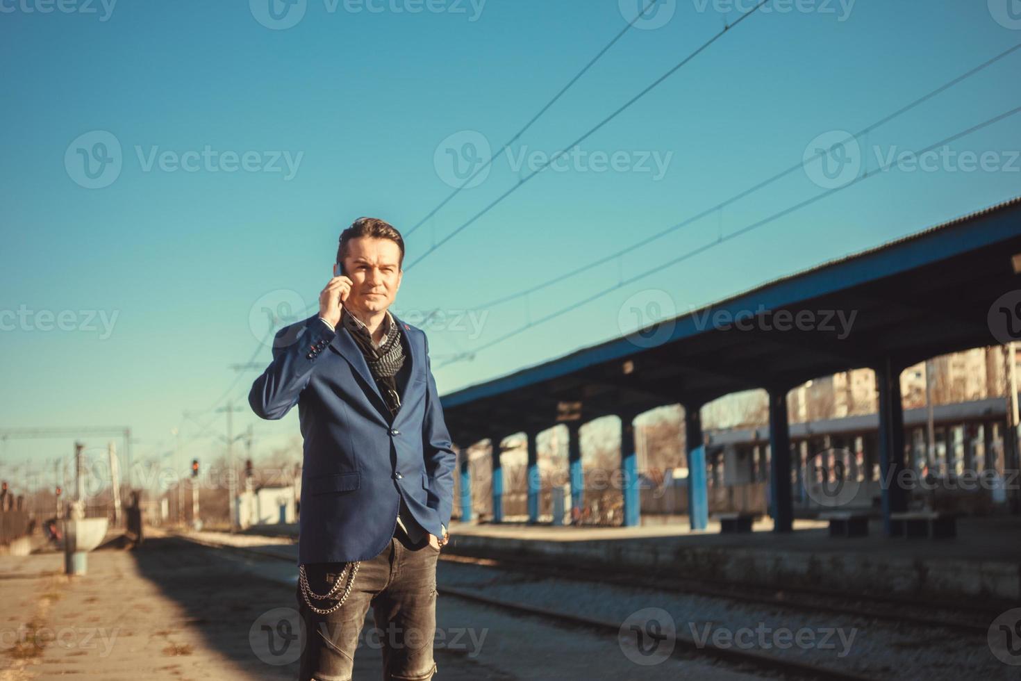 hombre de negocios adulto medio haciendo una llamada telefónica mientras espera en la estación de tren. foto