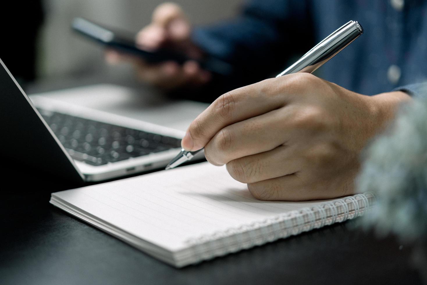 Man hand with pen writing on notebook with computer laptop at desk. photo