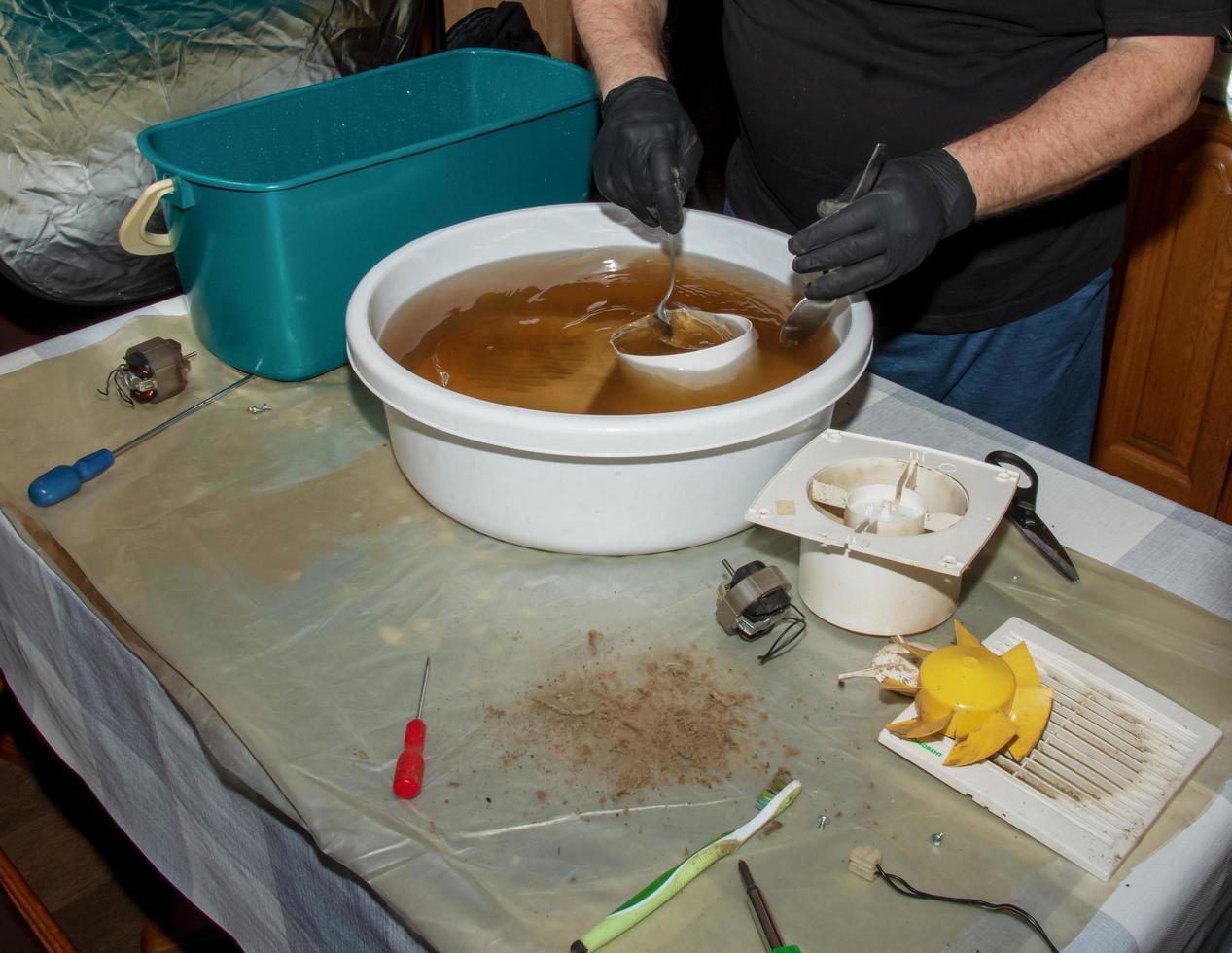Washing the plastic parts of a very dirty kitchen exhaust fan in an aqueous solution of sodium hydroxide. A man works in protective gloves. photo
