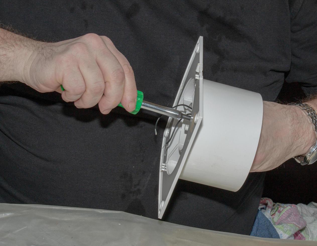 The process of assembling the kitchen exhaust fan after cleaning the wash. A man works with a screwdriver in his hands photo