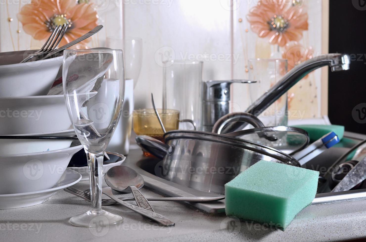 A huge pile of unwashed dishes in the kitchen sink and on the countertop photo