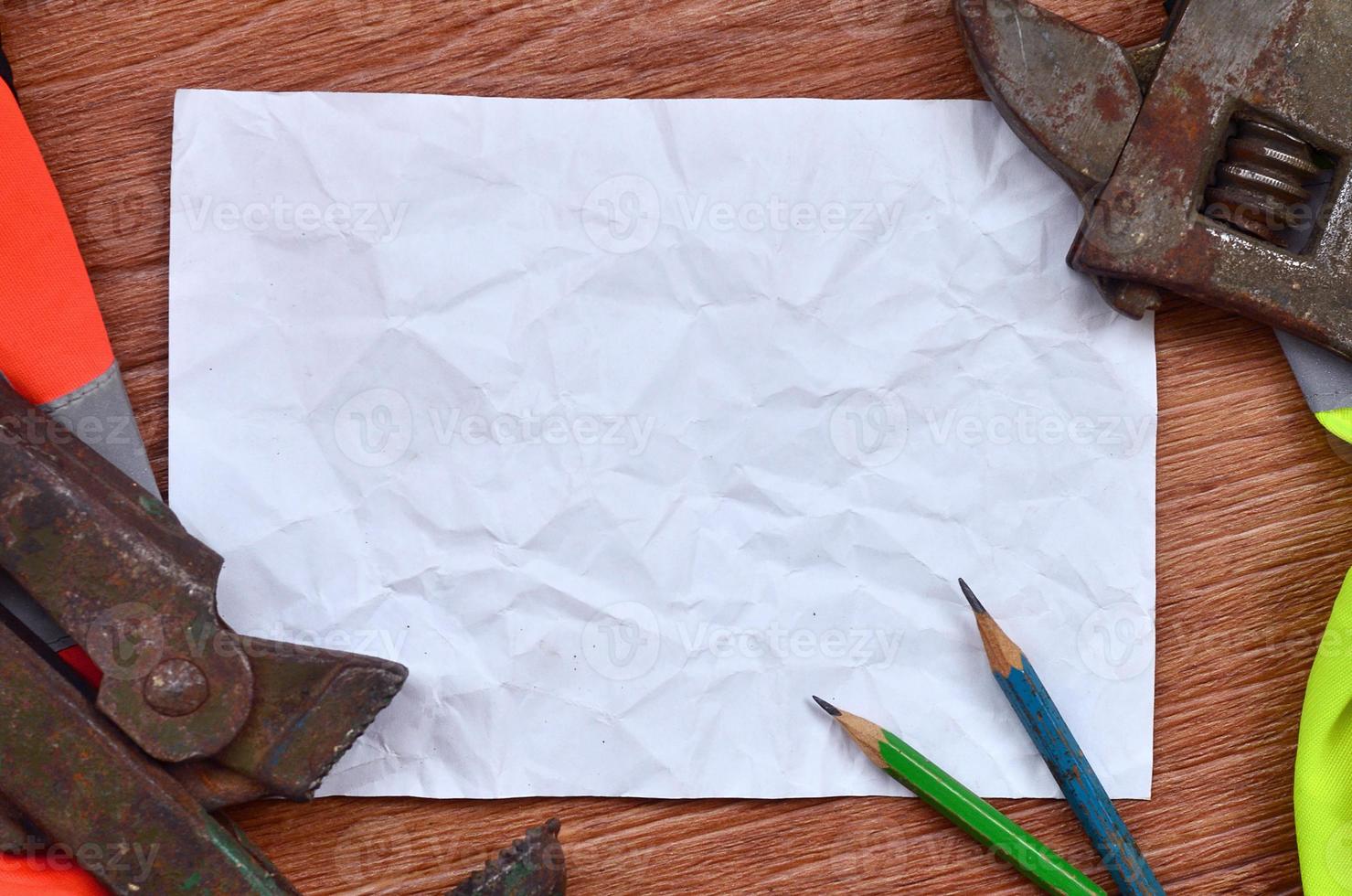 A crumpled sheet of paper with two pencils surrounded by green and orange working uniforms and adjustable wrenches photo