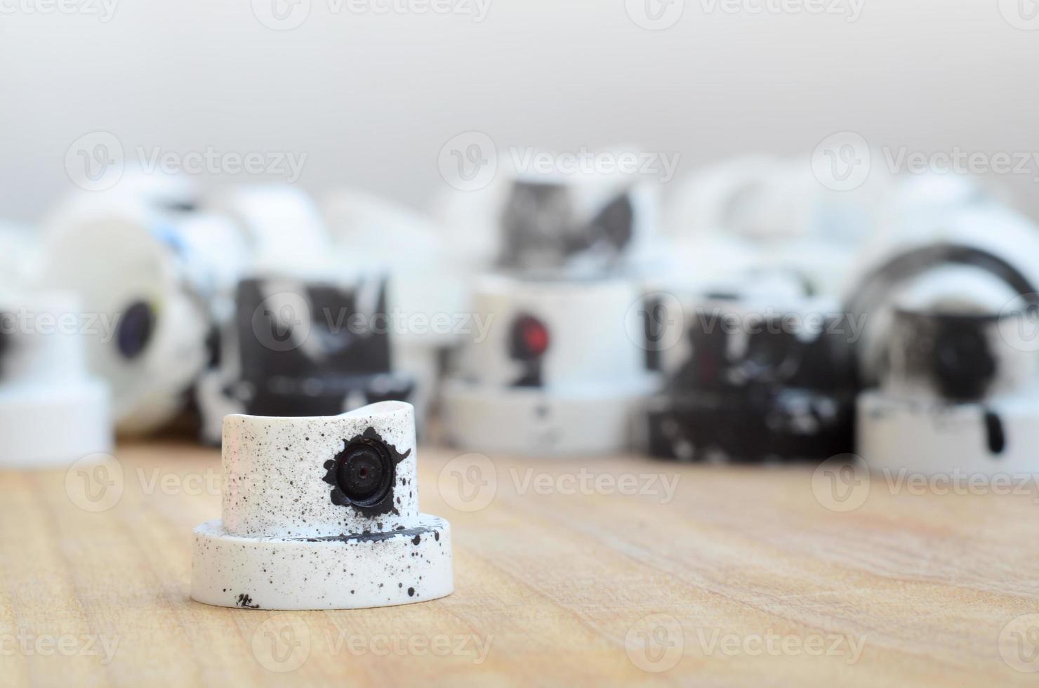 Several plastic nozzles from a paint sprayer that lie on a wooden surface against a gray wall background. The caps are smeared in black paint. The concept of street art and graffiti photo