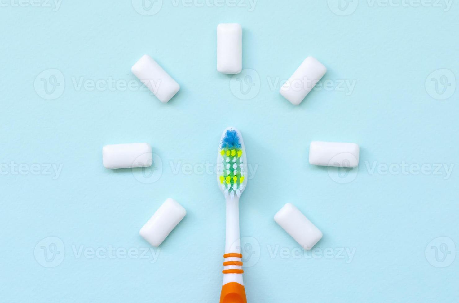 el cepillo de dientes y las gomas de mascar se encuentran sobre un fondo azul pastel. vista superior, endecha plana. concepto mínimo foto