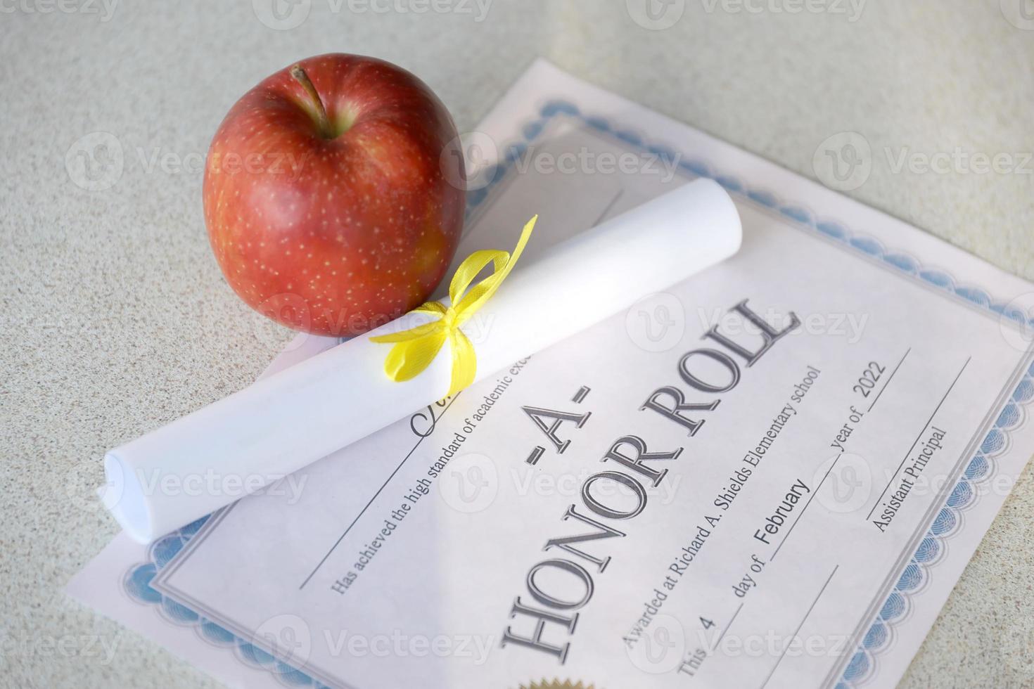 un cuadro de honor se encuentra en la mesa con un pequeño pergamino y una manzana roja. documentos educativos foto
