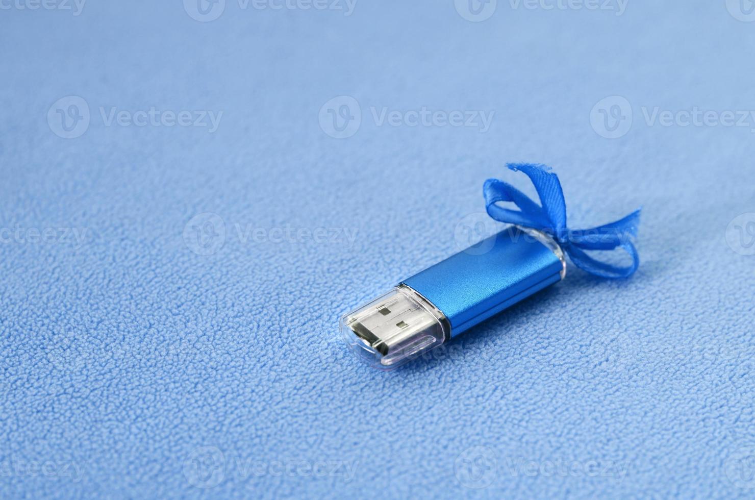 Brilliant blue usb flash memory card with a blue bow lies on a blanket of soft and furry light blue fleece fabric. Classic female gift design for a memory card photo