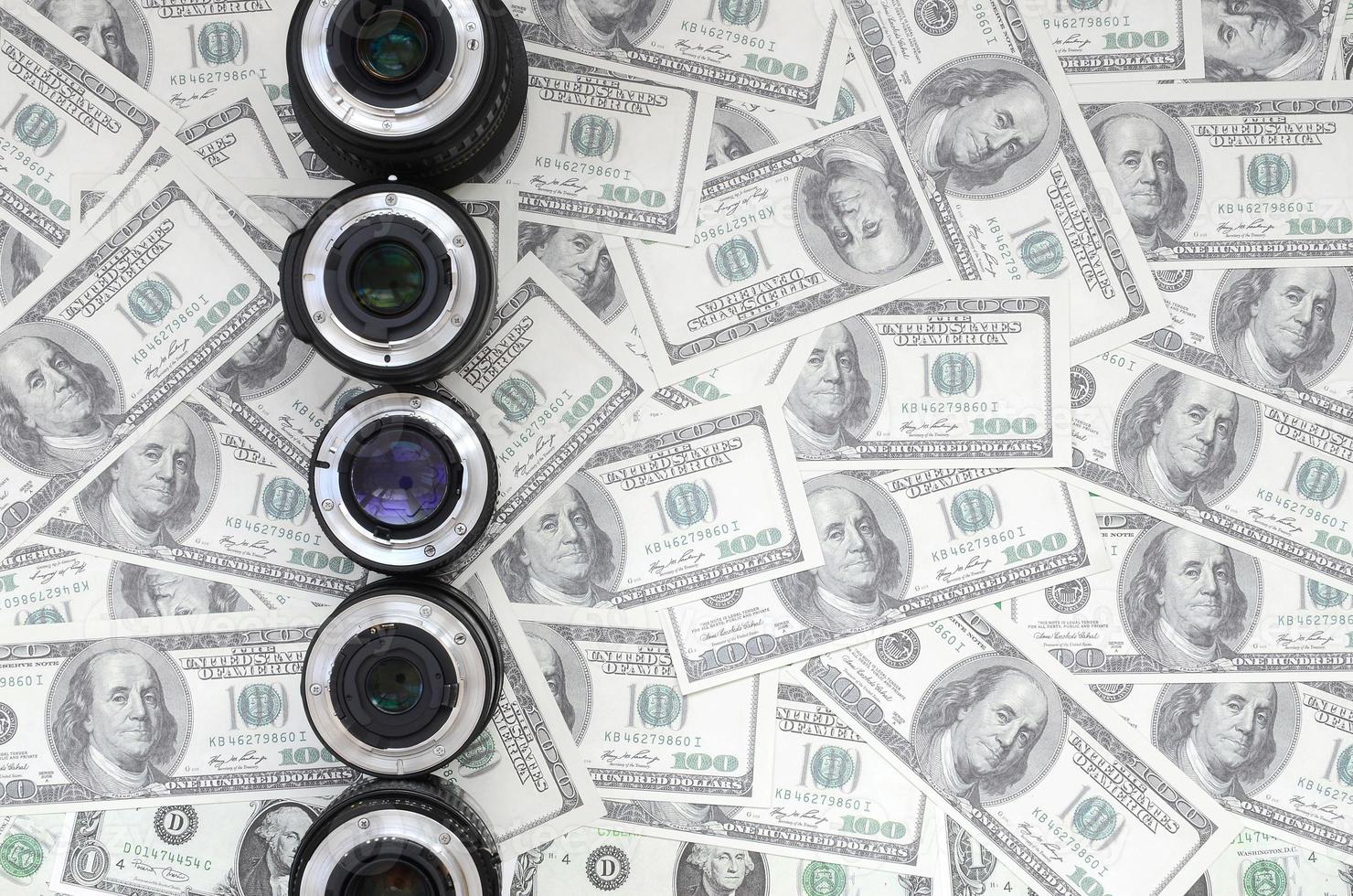 A few photographic lenses lies on the background of a lot of dollar bills. Space for text photo