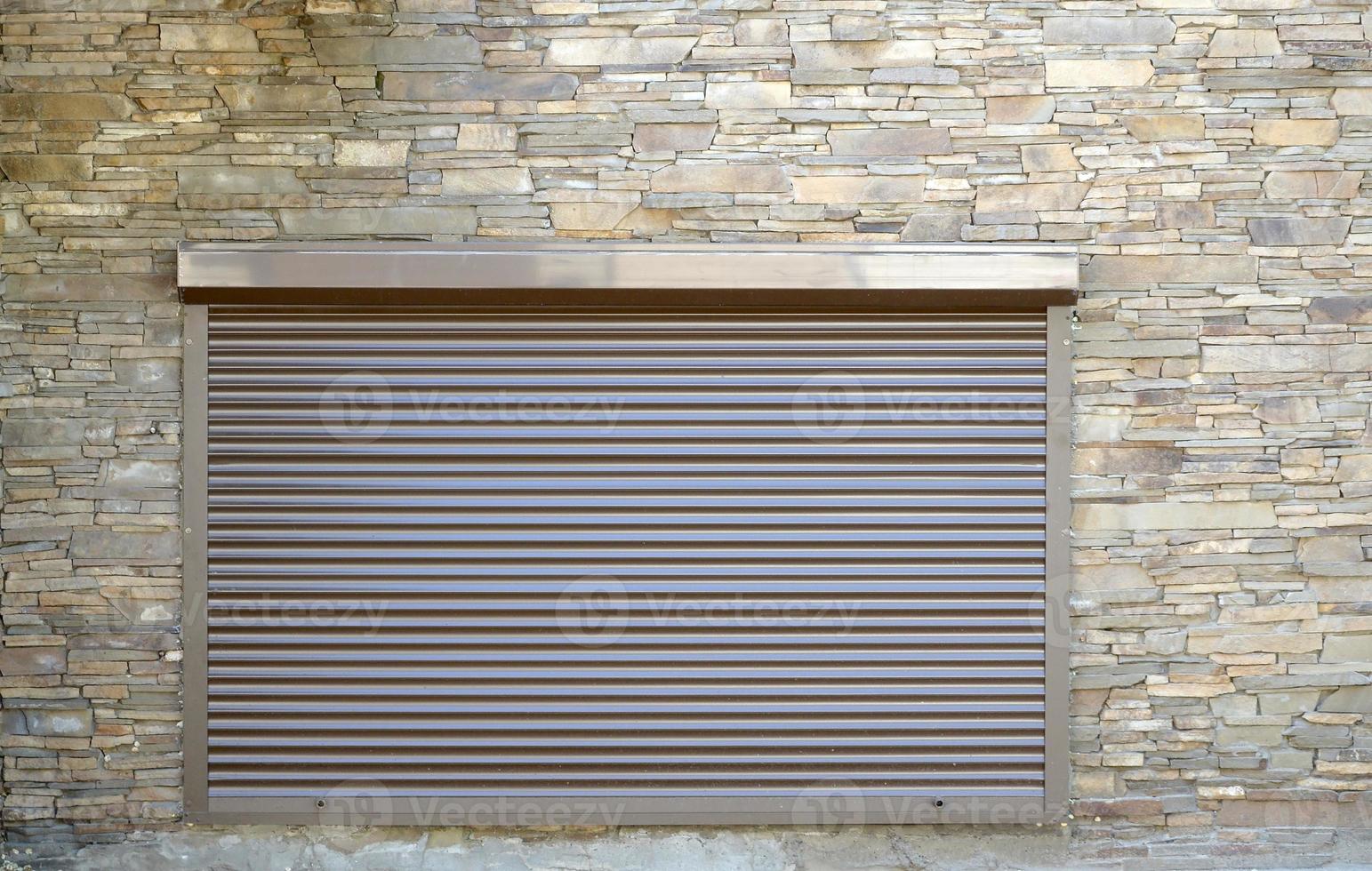 A window with brown metal rolling shutters and wall decoration with artificial stone photo