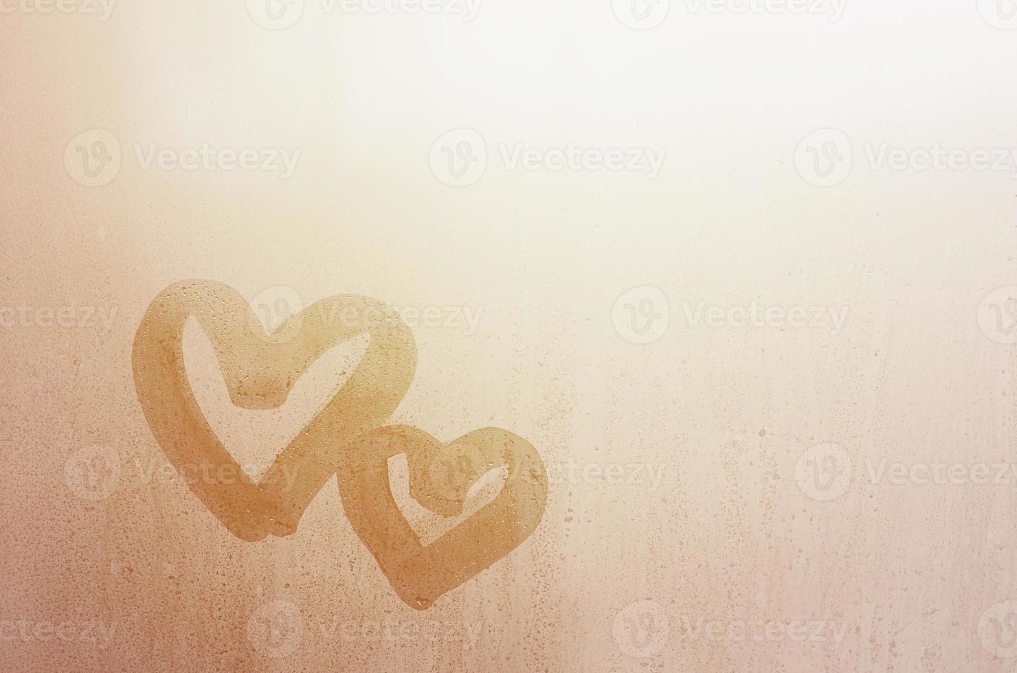 Couple of abstract blurred love heart symbol drawn by hand on the wet window glass with sunlight background. Template for Valentine Day postcards photo