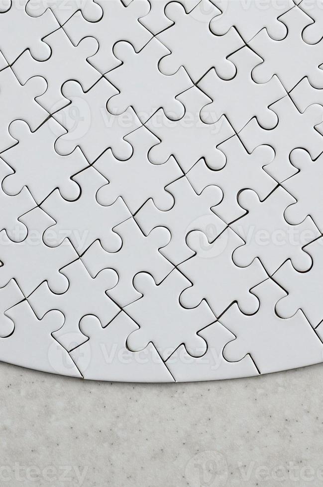 A white jigsaw puzzle in the complete form lies on a treated stone surface. Textured image with copy space photo