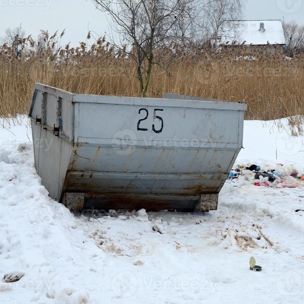 Trash bin at the side of street in winter with lip garbage container winter snow. Metal container for household waste photo