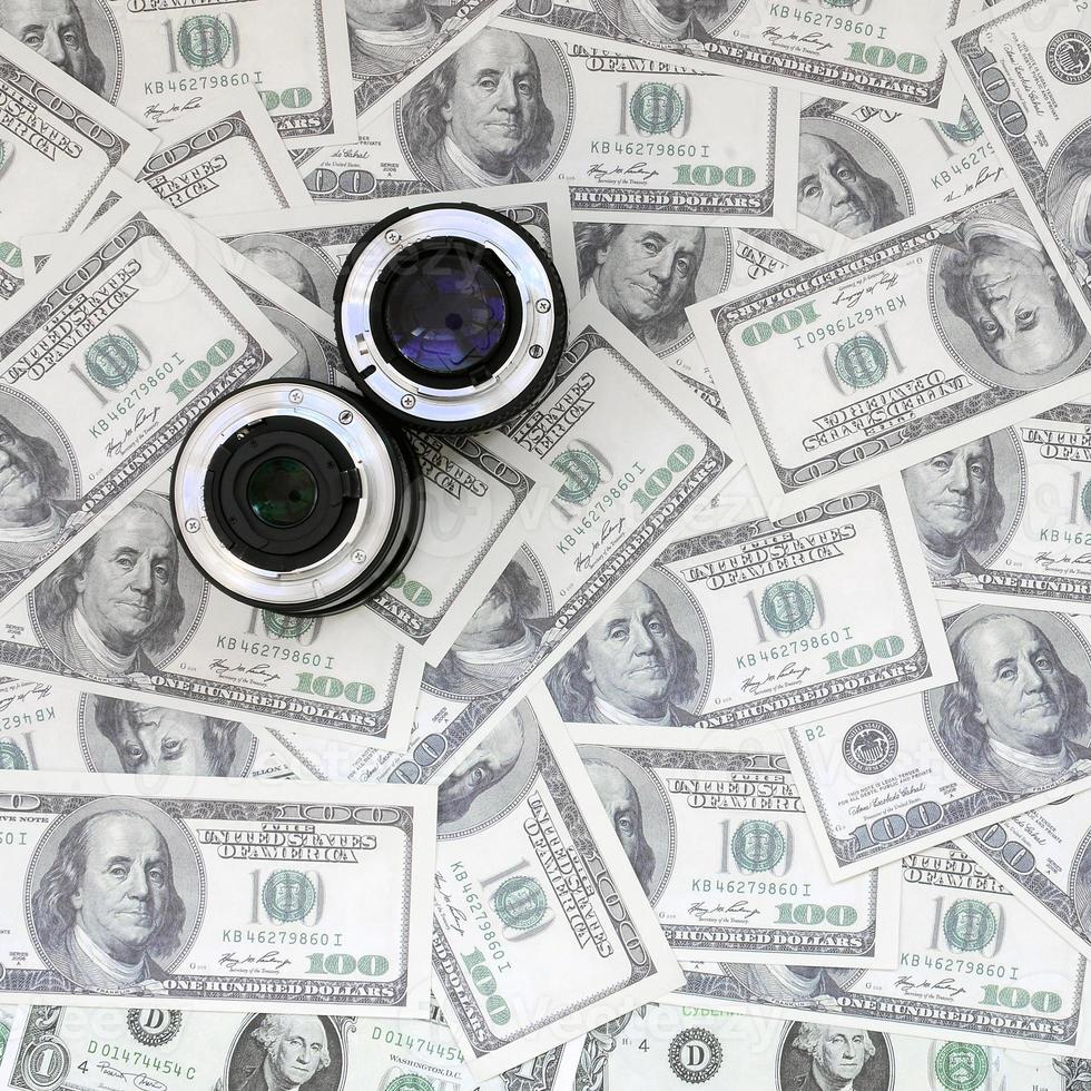 Two photographic lenses lie on the background of a lot of dollar bills. Space for text photo